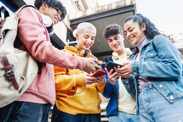 University students watching digital smart mobile phones at college campus. Group of Teenager friends using cellphones sharing content on social media app - 写真・画像