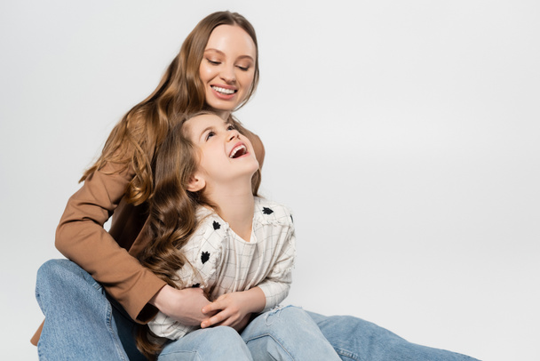 happy woman embracing laughing daughter isolated on grey - Photo, Image