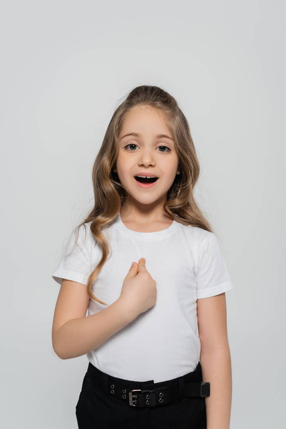 здивована дівчина в білій футболці, вказуючи пальцем на себе ізольована на сірому
 - Фото, зображення