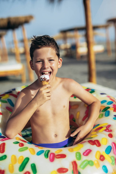 Młody chłopak na plaży je lody w letni dzień i dobrze się bawi. - Zdjęcie, obraz
