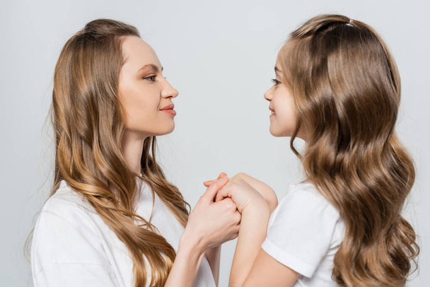 side view of girl and woman looking at each other and holding hands isolated on grey - Foto, immagini