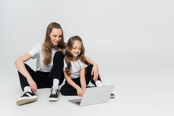 onnellinen äiti ja tytär katsomassa elokuvaa kannettavalla tietokoneella harmaalla taustalla  - Valokuva, kuva