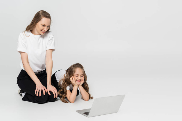 cheerful mother and daughter watching movie on laptop on grey background  - Photo, image
