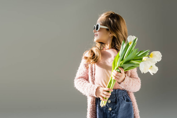 happy kid in sunglasses holding flowers isolated on grey  - Foto, afbeelding