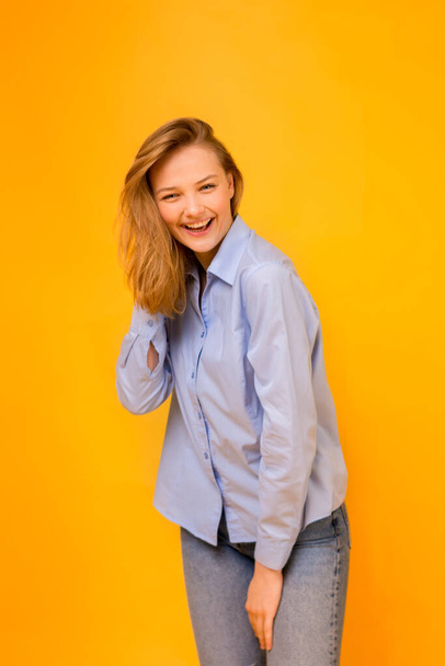 Emoties van geluk en succes. Gelukkig lachend meisje in een blauw shirt en blauwe jeans op een gele achtergrond. Kleurenschema van de Oekraïense vlag. - Foto, afbeelding