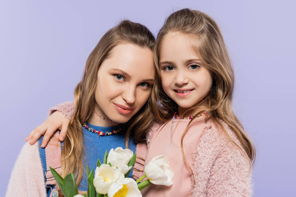 woman holding tulips near smiling daughter isolated on purple  - Photo, Image