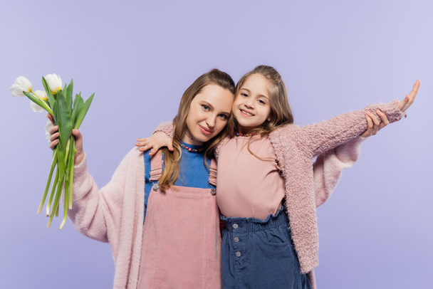 woman holding tulips near smiling daughter with outstretched hand isolated on purple  - Foto, Imagem