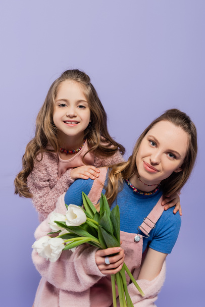 smiling woman holding tulips near happy daughter isolated on purple  - Foto, Imagen