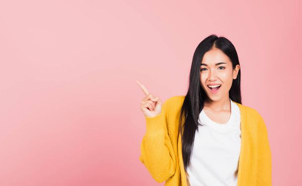 Portrait Asian beautiful young woman smiling standing pointing finger out on pink background, Thai happy face excited female point into empty looking to camera with copy space for text - Foto, imagen