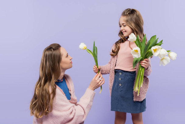 smiling woman receiving tulip and looking at happy daughter isolated on purple  - Photo, Image