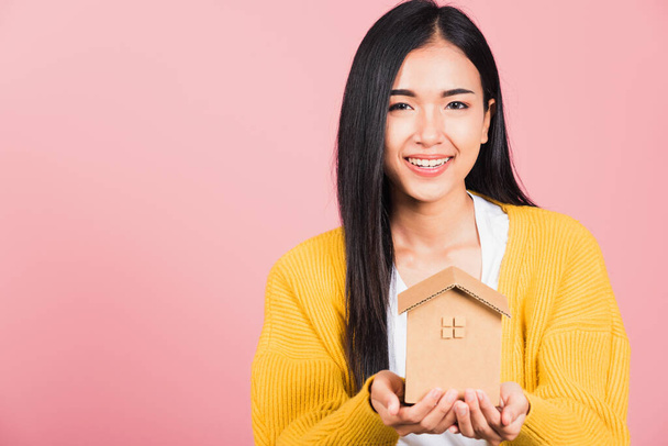Happy Asian portrait beautiful cute young woman excited smiling holding house model on hand, studio shot isolated on pink background, broker female hold home real estate insurance and banking concept - 写真・画像