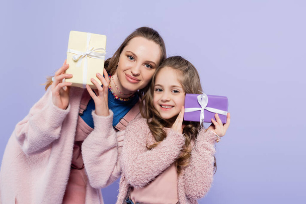 feliz niño y alegre madre sosteniendo regalos aislados en púrpura - Foto, Imagen