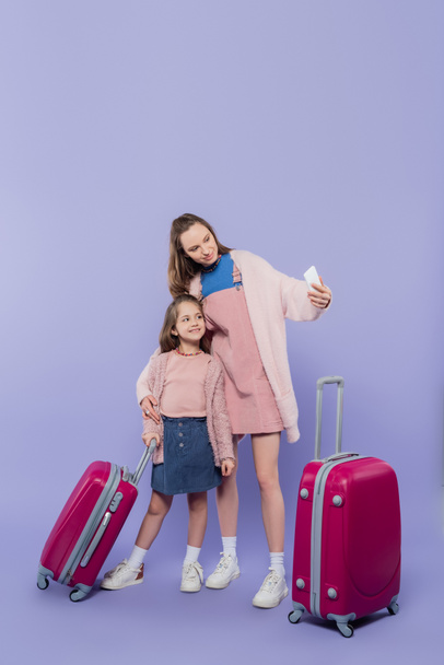 full length of happy mother and child taking selfie near baggage on purple - Photo, Image