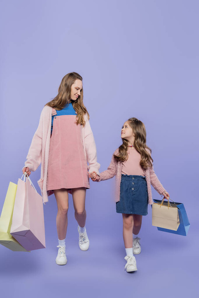 full length of mother and daughter holding shopping bags while walking on purple - Foto, immagini
