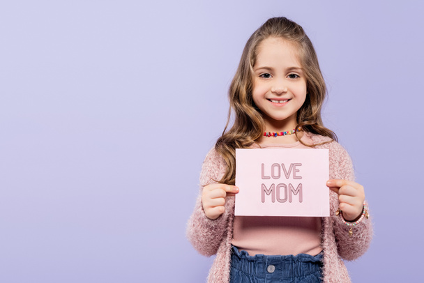 happy kid holding greeting card with love mom lettering isolated on purple  - Fotoğraf, Görsel