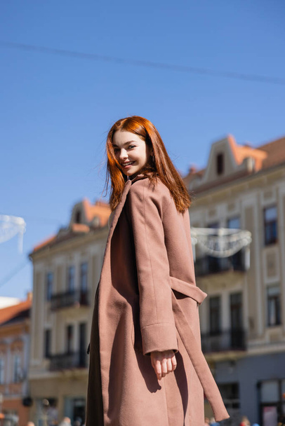 joyful redhead woman in coat on street of european city  - Foto, Bild