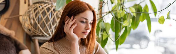 young redhead woman holding hand near cheek in cafe, banner - Foto, imagen