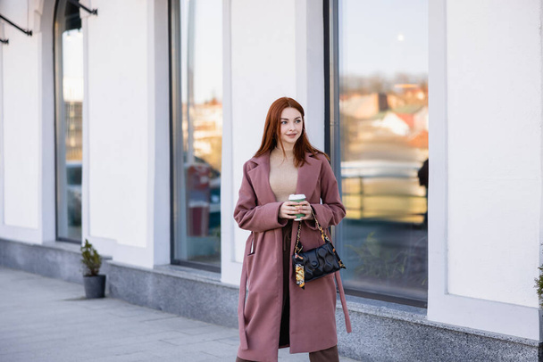redhead young woman with handbag holding paper cup on street  - Fotó, kép