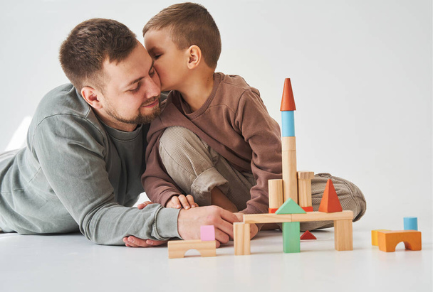 Jóképű fiú megcsókolja az apját. Apaság. Apa és fia játszik színes fa blokkok fehér háttér - Fotó, kép
