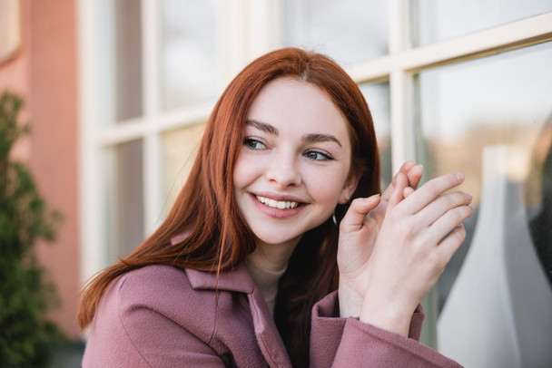 portrait of young cheerful woman in coat looking away outside - Photo, image