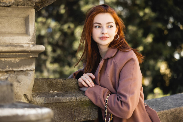 portrait of young redhead woman in coat looking away outside - 写真・画像