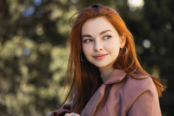 portré boldog vörös hajú nő kabátban néz félre  - Fotó, kép