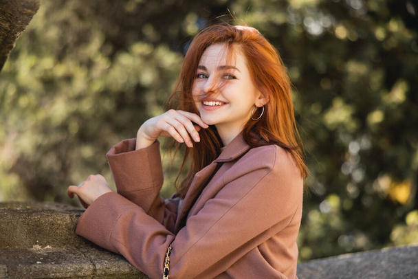 portrait of positive redhead woman in coat posing outside  - Valokuva, kuva