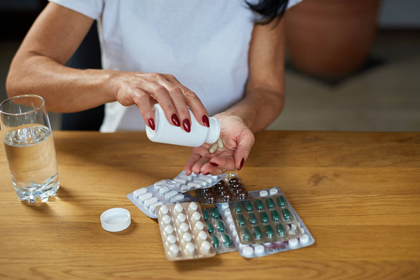 Зрелая больная женщина, принимающая антибиотики, таблетки аспирина из бутылки от гриппа, холодного или сезонного вируса, концепция здравоохранения и лечения - Фото, изображение