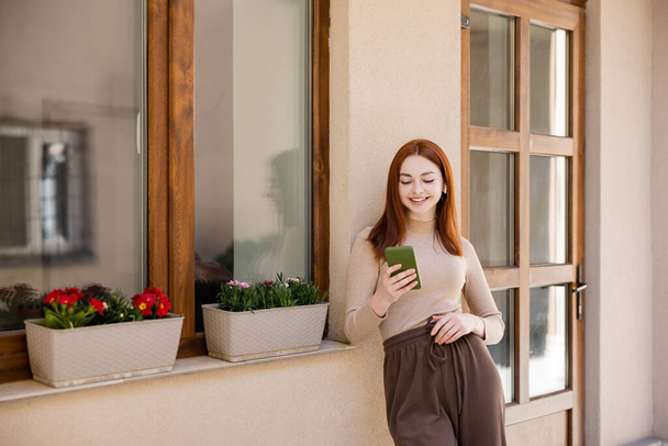 pleased redhead woman in wireless earphone holding smartphone and listening music  - Foto, imagen