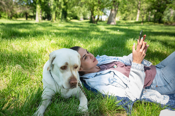 Молодая красивая женщина в парке со своей домашней собакой белый лабрадор ретривер, который она принимает из приюта для домашних животных, чтобы дать ему хорошую жизнь и любовь. Женщина-любительница животных со своим приёмным щенком развлекается. - Фото, изображение