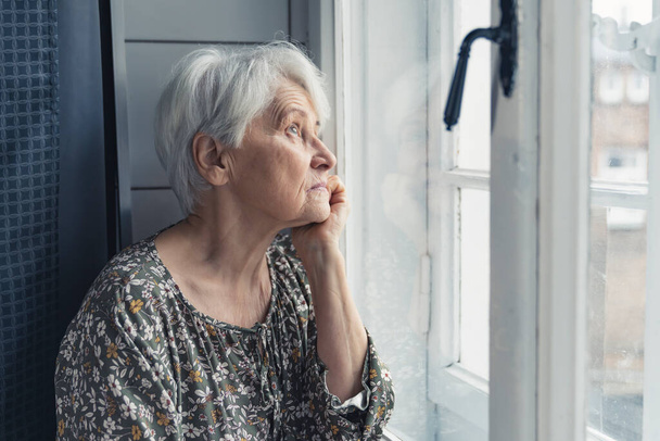 sad European grandma looking out of the window - 写真・画像