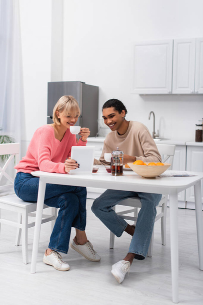 happy african american man and cheerful woman looking at digital tablet during breakfast - 写真・画像