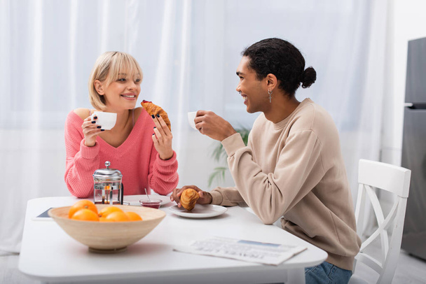 happy multiethnic couple holding croissants during breakfast in morning  - Valokuva, kuva