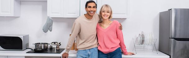 ευτυχισμένο πολυεθνικό ζευγάρι στέκεται στη σύγχρονη κουζίνα, πανό - Φωτογραφία, εικόνα