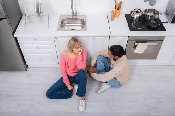 top view of happy multiethnic couple sitting on floor in modern kitchen  - Photo, image