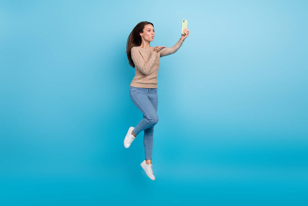 Photo of romantic lady jump hold phone make selfie send air kiss wear beige sweater isolated blue color background - Photo, Image