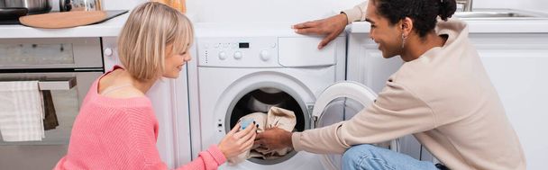 glückliches gemischtrassiges Paar legt Kleidung in Waschmaschine, Banner - Foto, Bild