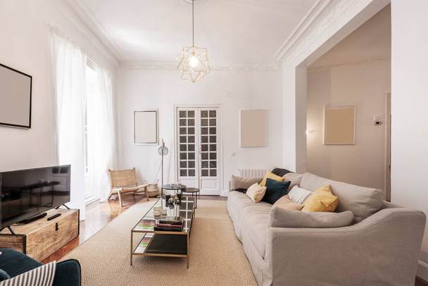 Obývací pokoj s třísedačkovou pohovkou potaženou látkou s mnoha polštáři, kovovým konferenčním stolkem a zrcadly a dřevěnými dveřmi, světlým kobercem na podlaze a televizí na jedné stěně - Fotografie, Obrázek