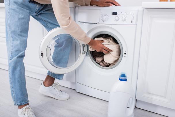 обрізаний вид афроамериканця, який кладе одяг у пральну машину
 - Фото, зображення