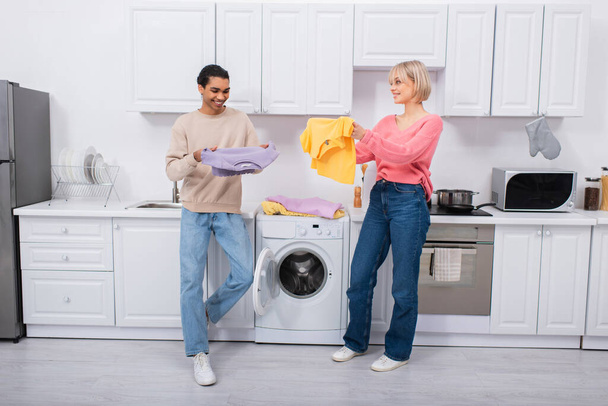 happy interracial couple holding clean and colorful clothes  - Foto, Bild
