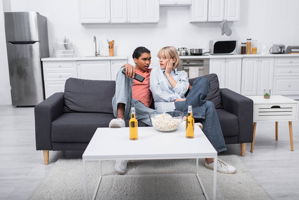 young interracial couple looking at each other while watching movie in living room - Foto, Imagen