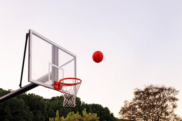 ball flying to a basketball hoop with the sky in the background, concept of urban sport outdoors, copy space for text - Фото, изображение