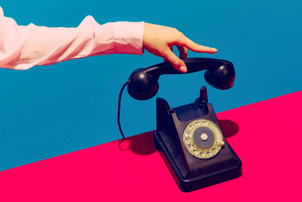 Retro objects, gadgets. Female hand holding handset of vintage phone isolated on blue and pink background. Vintage, retro fashion style. Pop art photography. - Foto, imagen