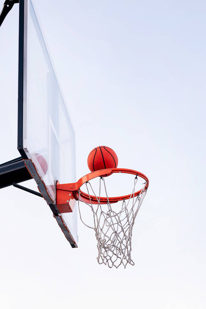 ball entering in a basketball hoop with the sky in the background, concept of urban sport outdoors, copy space for text - Photo, Image