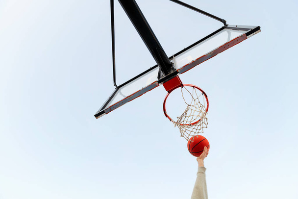 view from below of a hand shooting a basket in a basketball hoop with the sky in the background, concept of urban sport outdoors, copy space for text - Photo, image