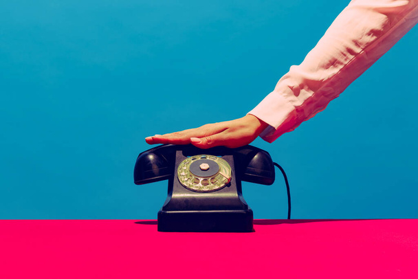 Retro objects, gadgets. Female hand holding handset of vintage phone isolated on blue and pink background. Vintage, retro fashion style. Pop art photography. - Zdjęcie, obraz