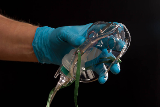 Βοήθεια για ασθενείς με Covid - χέρι γιατρού σε ιατρικά γάντια με μάσκα οξυγόνου μίας χρήσης για υποστήριξη της αναπνοής - Φωτογραφία, εικόνα
