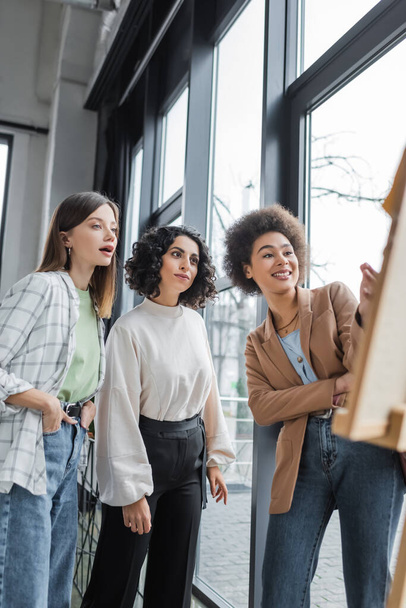 Interracial businesswomen looking at blurred board in office  - 写真・画像