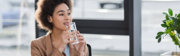 Positive african american businesswoman holding glass of water in office, banner  - Fotografie, Obrázek