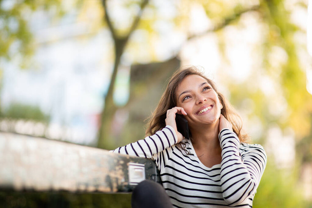 Portret szczęśliwej młodej kobiety rozmawiającej przez komórkę w parku - Zdjęcie, obraz